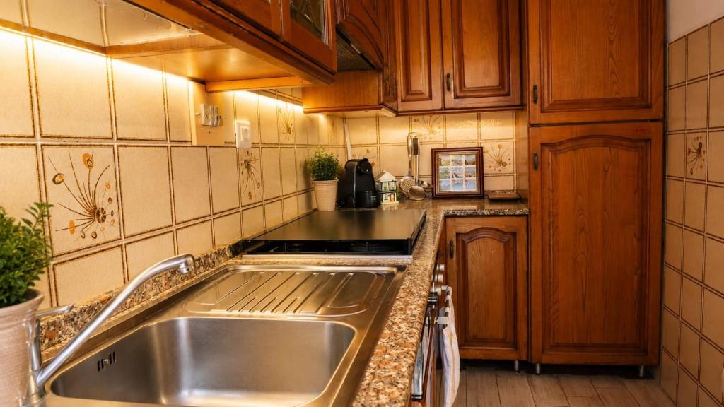 A warmly lit kitchen with wooden cabinets, tiled walls, a granite countertop, and a stainless-steel sink.