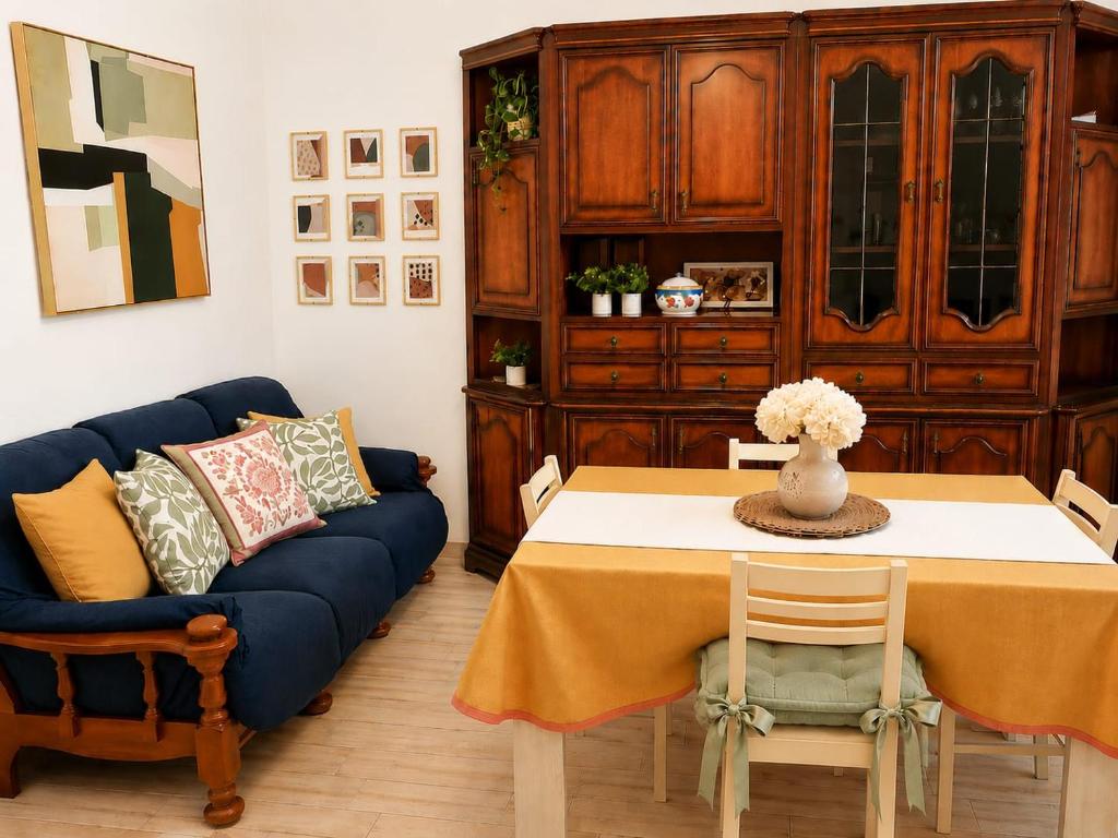 A dining and sitting room with a table, upholstered chairs, blue sofa, artwork, and a large wooden cabinet.