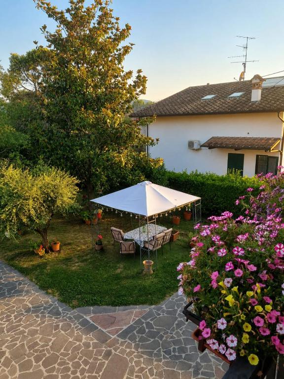 A sunlit garden patio with a white umbrella, outdoor table and chairs, flowering plants, and a house in the background.